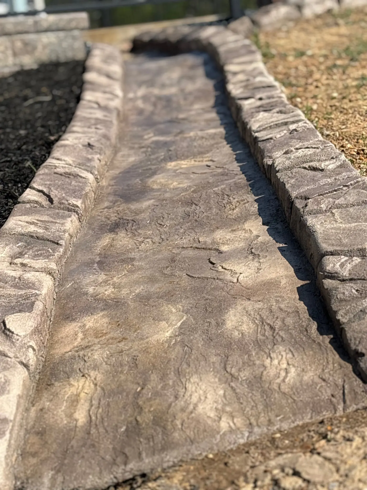 Decorative stamped concrete curbing edging a manicured flower bed installed by The Muscle